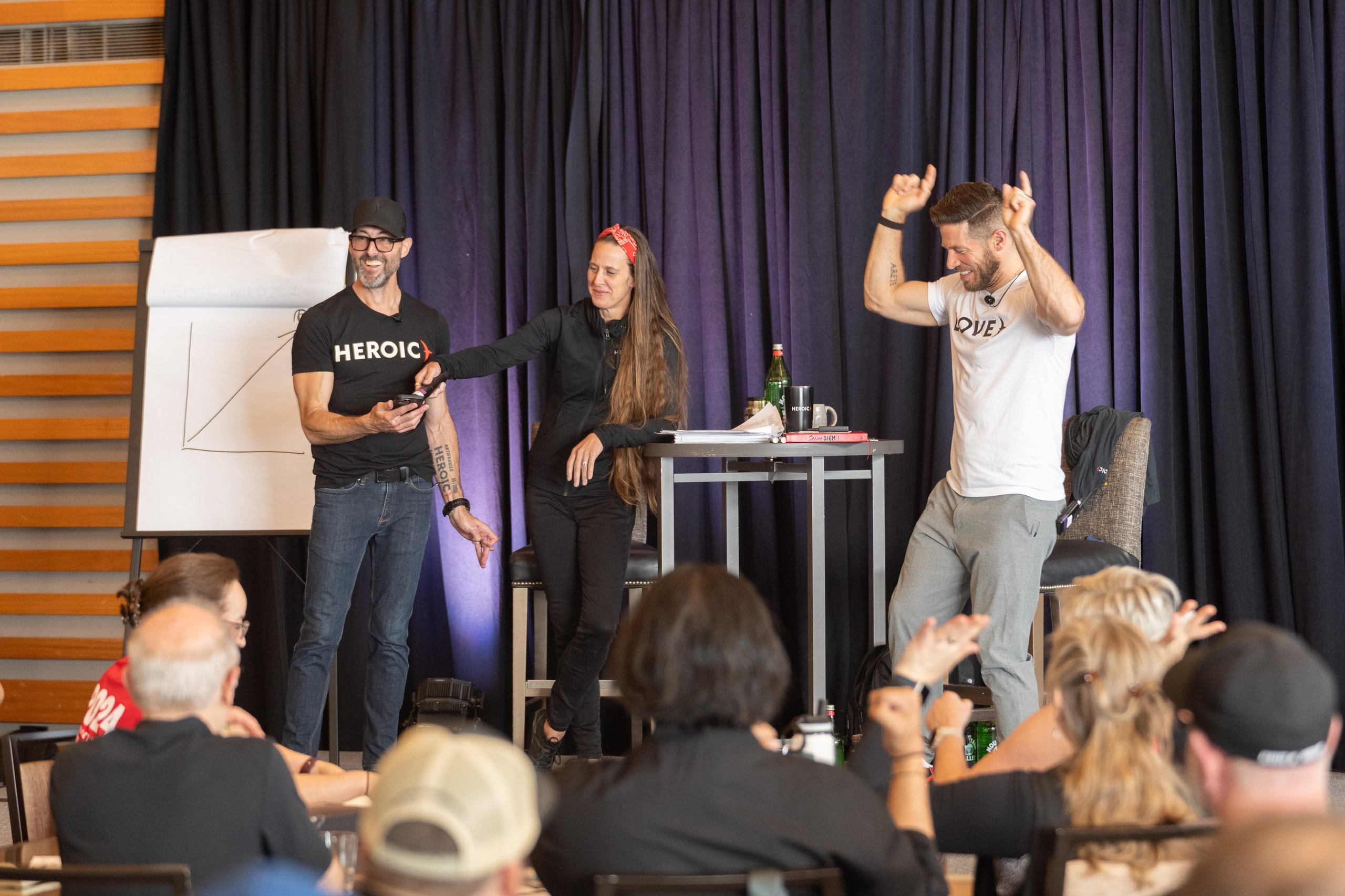 Heroic coaches mid-workshop — one pointing skyward as the room lights up