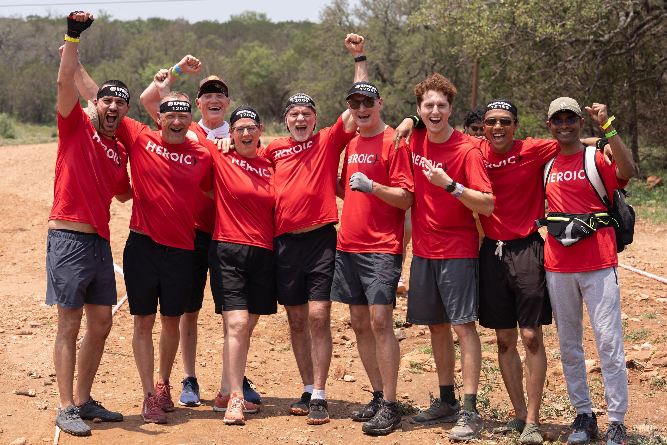 A team of Heroic members in matching shirts, fists raised at a Spartan race finish